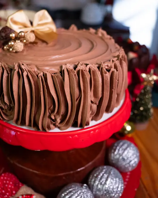 Bolo tronco de chocolate com cobertura de chocolate em relevo e laço dourado, sobre boleira vermelha